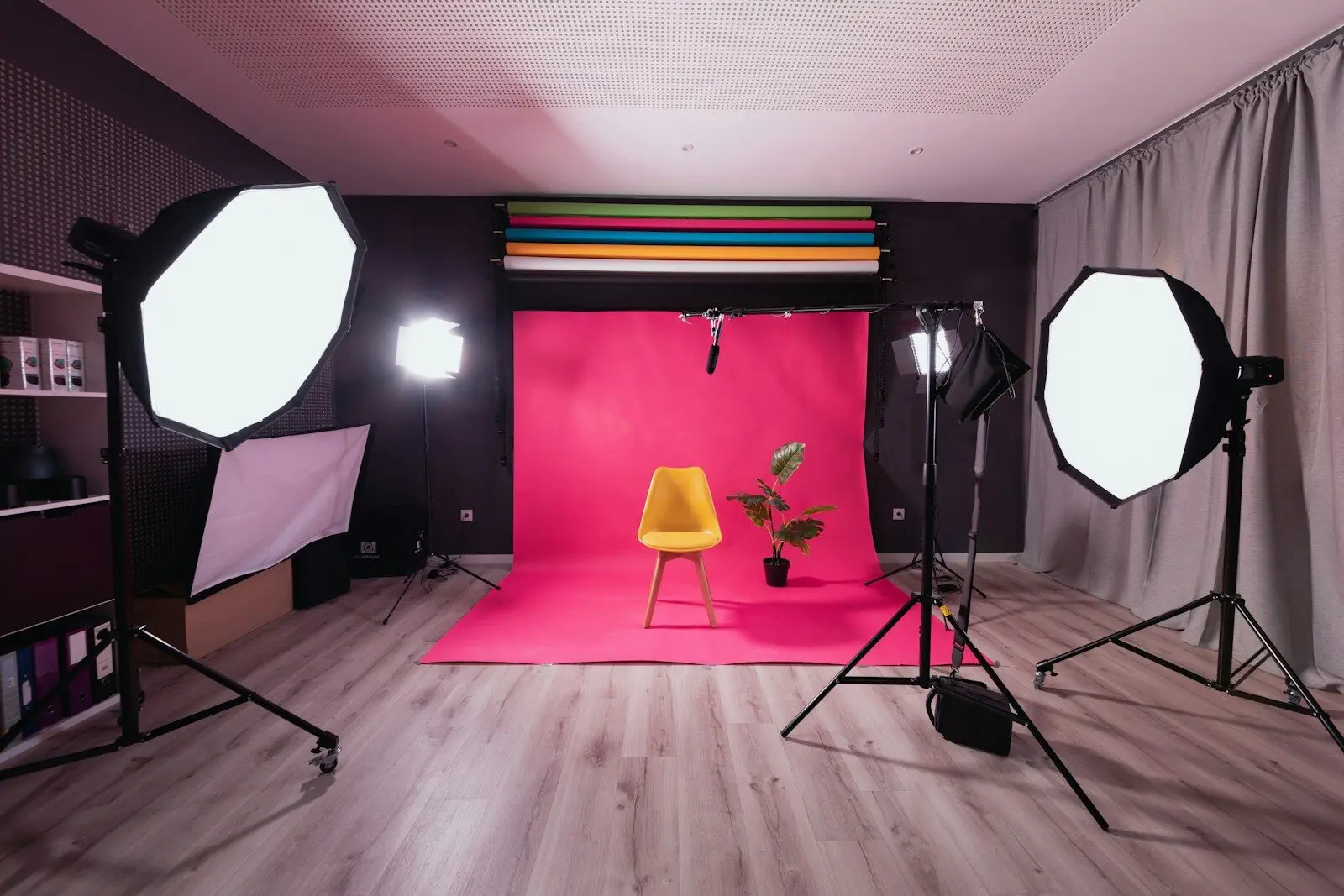 Estúdio fotográfico com fundo rosa, cadeira amarela e iluminação profissional