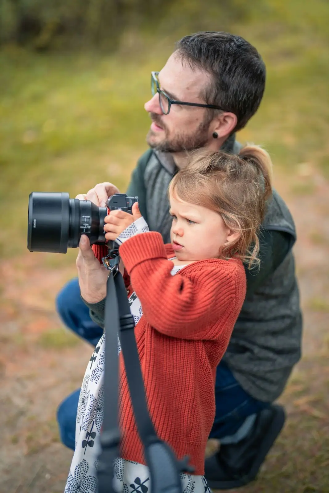 Pai ajudando a filha pequena a segurar uma câmera fotográfica